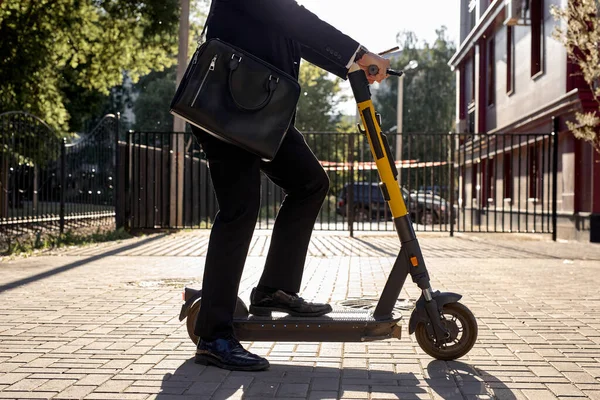 Обрізаний бізнесмен в центрі міста, в офіційному костюмі тримає ноутбук мішок їзда скутер — стокове фото