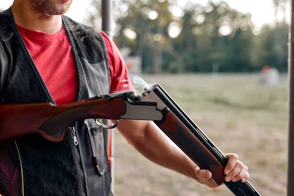 Cropped young man charges pump-action shotgun in an outdoor range.