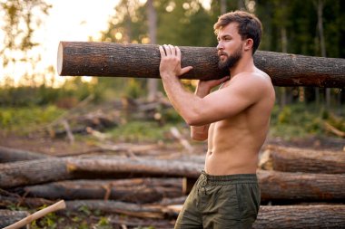 Genç erkek omuzlarında büyük bir kütük taşır ve ormanda ilerler.