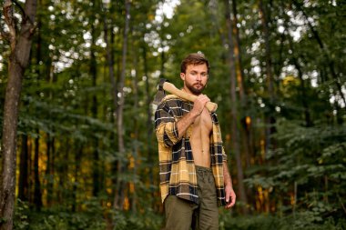 Sakallı, kendine güvenen, açık ekose gömlekli beyaz adam büyük bir balta taşıyor.