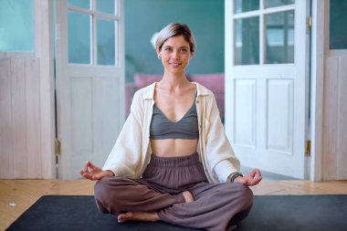 Rahatlamış atletik genç bayan içeride fitness minderinde oturuyor. Bayan Egzersiz Yapıyor.