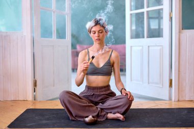 Aromatik bir Hint çubuğu yanıyor, güzel bir kadın evde meditasyon yapıyor, dinleniyor.