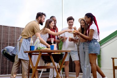 Arka bahçedeki terasta hamburger yiyen bir grup genç arkadaş.