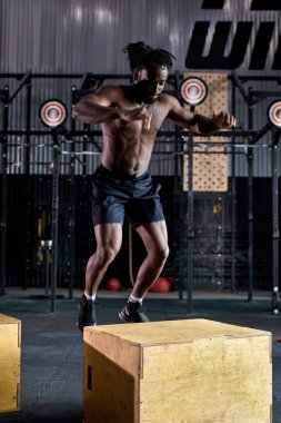 Genç, güçlü, terli, kaslı, iri kaslı, atlama egzersizi yapan bir afro adam.