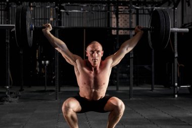 Genç sağlıklı erkek sporcu modern koyu renk spor salonunda ağır halterle egzersiz yapıyor..