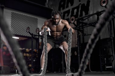 Savaş halatıyla aktif bir Afrikalı, spor salonunda egzersiz yapıyor.