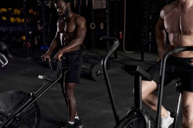 Modern spor salonunda egzersiz bisikleti kullanan genç ve güçlü adamlar. Bisiklet kullanan fitness erkeği