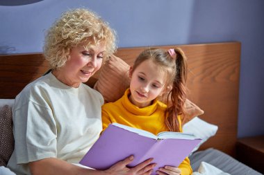 Büyükanne, çocuk kızına masal okur. Sıcak çocuk odasında yatakta yatar.