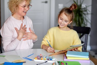 Kız el yapımı kartpostal hazırlarken kıdemli kadın tatlı torunuyla oturuyor.