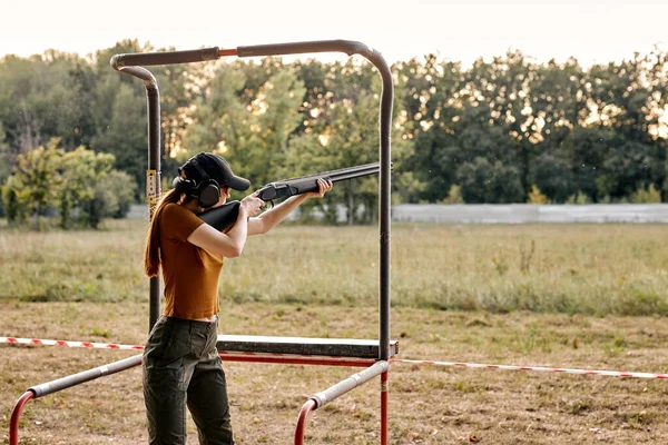 Jovem caucasiana fêmea em óculos e fone de ouvido apontando rifle ao lado, pronto para atirar. — Fotografia de Stock