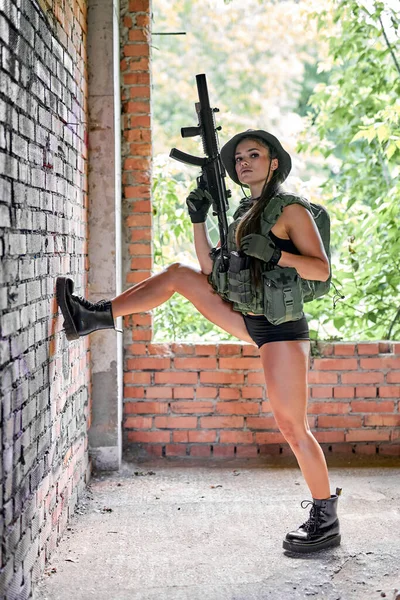 Sexy mujer caucásica en ropa militar con rifle posando en la cámara, levantando las piernas — Foto de Stock