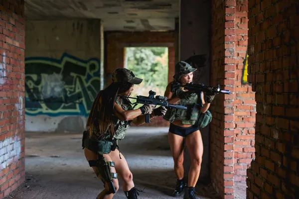 Két erős nő katona fegyvert fog és besétál az épületbe, bemennek a védelmi bázisra. — Stock Fotó