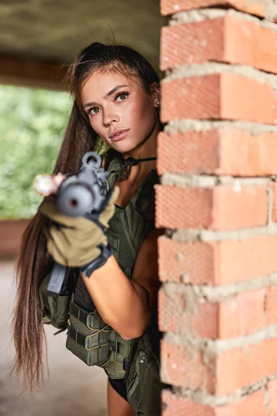 Mujer seria en desgaste militar está mirando al enemigo objetivo a través de la puerta — Foto de Stock