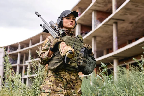 Femme militaire en équipement tactique posant pour photo dans l'herbe à côté du bâtiment abandonné — Photo