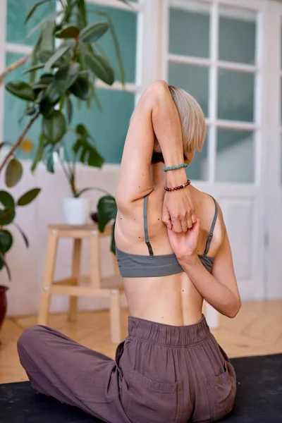 Evdeki yoga egzersizleri sırasında kollarını ve omurgasını esneten genç bir kadına arkadan bakmak. — Stok fotoğraf