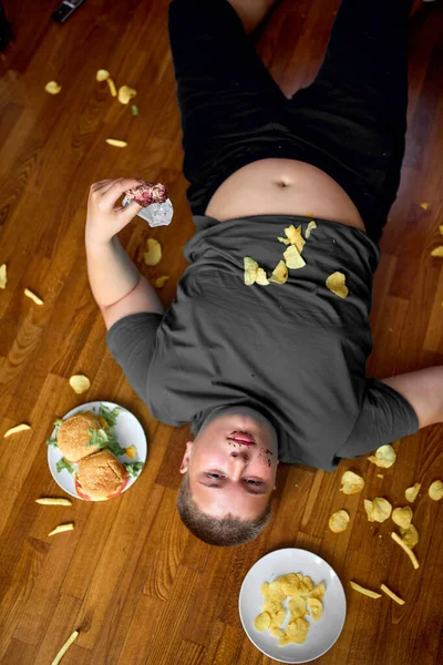 Top uitzicht op overeten jongen liggend op de vloer in de woonkamer, jonge Kaukasische tiener jongen — Stockfoto