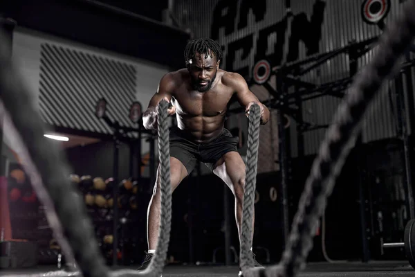 Hombre africano activo con cuerda de batalla haciendo ejercicio en el gimnasio de fitness de entrenamiento funcional — Foto de Stock
