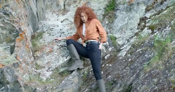 Giovane bella rossa femmina in camicia casual in posa in montagna, alzando una gamba — Video Stock