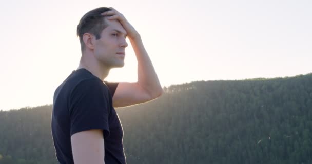 Впевнений красивий чоловік стоїть в горах сам, дивлячись на сторону — стокове відео