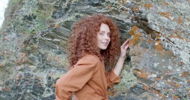 Joven hermosa pelirroja hembra en camisa casual posando en las montañas, junto a las rocas — Vídeos de Stock