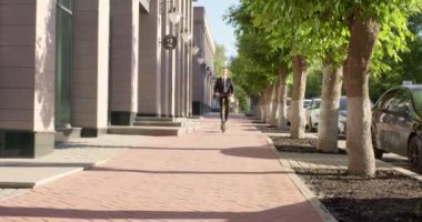 Sokakta elektrikli scooter kullanan, takım elbiseli yakışıklı, mutlu bir adam.