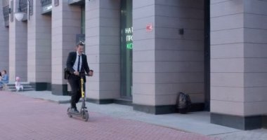 Şehirdeki işe giderken elektrikli scooter kullanan işadamı eğleniyor.