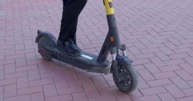 Elinde bir fincan kahve, elinde scooter 'la caddeye bakan bir erkek.