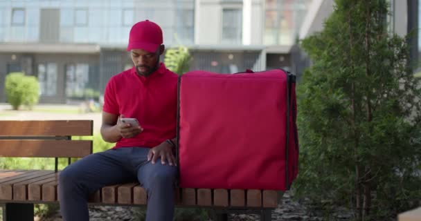 Uomo nero consegna ottenere messaggio dal cliente su smartphone, felice di andare a consegnare. — Video Stock