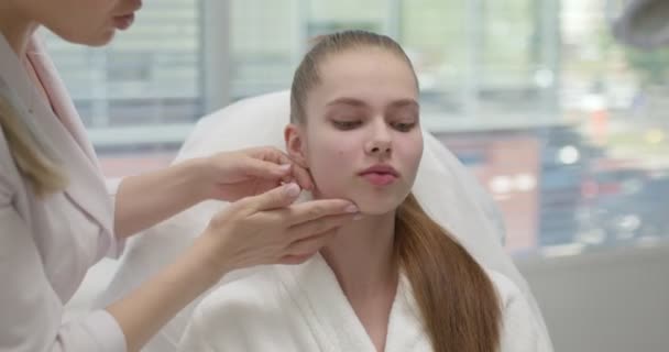 Kvinna kosmetolog tittar på fridfull ung kvinnlig ansikte kontroll hudåkomma — Stockvideo