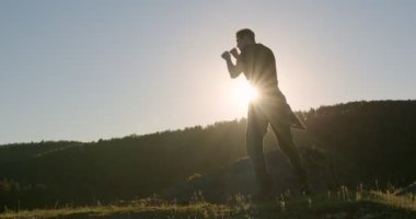 Güçlü bir adam doğada vücut dövüşü yapıyor. Dövüşçü eğitimi açık havada tekmeliyor.