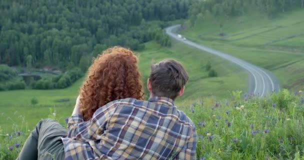 Vista trasera de la pareja sentada en el campo de las montañas mirando al lado en contemplación — Vídeo de stock