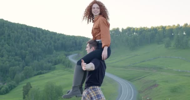 Сильный мужчина держит девушку на плечах, веселится в красивых горах — стоковое видео