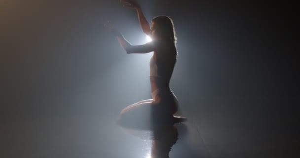 Bikini iç çamaşırlı model kadın, yerde, yağmur damlalarının altında, dumanlı, karanlık stüdyoda oturuyor. — Stok video