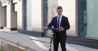 Takım elbiseli işadamı elektrikli scooterla dururken akıllı telefonla çalışıyor.