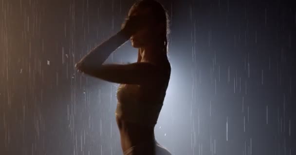 Wet woman silhouette standing on dark lithgted background in the pouring rain — Stock Video