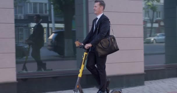 Zakenman paardrijden elektrische kick scooter op stadsgezicht achtergrond — Stockvideo