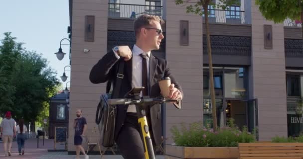 Cool snygg affärsman i sungalsses står utomhus med elektrisk skoter — Stockvideo