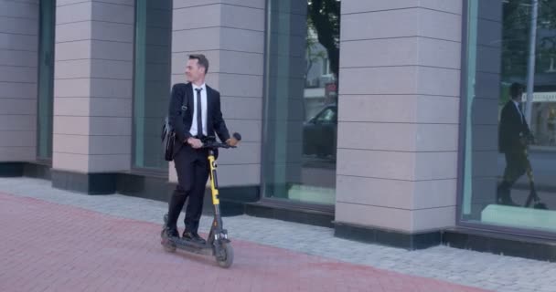 Hombre de negocios moderno montando scooter eléctrico mientras viaja al trabajo en la ciudad — Vídeos de Stock