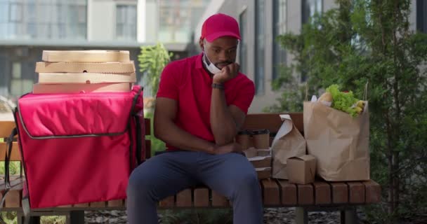 Entrega hombre afroamericano en uniforme rojo con bolso termo o mochila esperando a los clientes — Vídeos de Stock