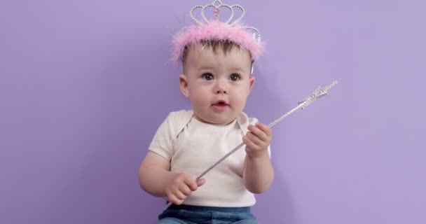 魔法の杖を手に持つ美しい小さな赤ん坊の女の子は、紫の上に隔離され、それを研究 — ストック動画