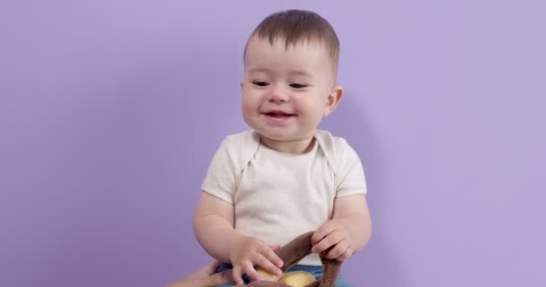 Медова маленька дівчинка сидить граючи з іграшкою в студії, ізольована на фіолетовому фоні — стокове відео