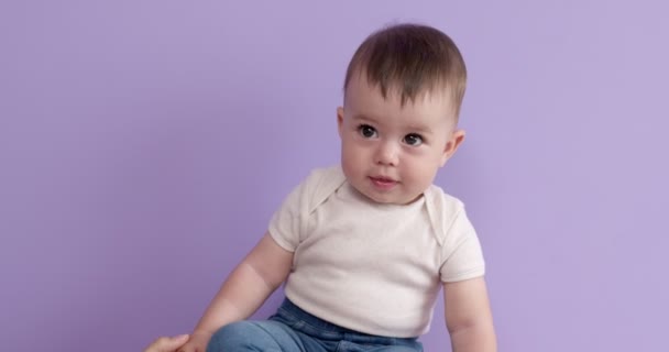 Mooi kind baby meisje glimlachen gelukkig kijkend naar kant, close-up, paarse achtergrond — Stockvideo