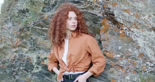Charmante schöne Rotschopf-Frau in lässigem Hemd posiert in den Bergen, neben Felsen — Stockvideo