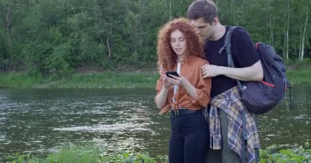 Bonita pareja caucásica discutiendo dónde ir, utilizando el mapa en línea en el teléfono inteligente — Vídeo de stock