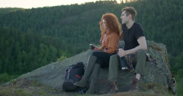 Utmattade par dricka te efter vandring, sitter på klippan i Mountain Cliff — Stockvideo