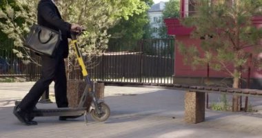 Şık bir erkek şehir merkezinde elektrikli scooter sürdükten sonra bankta dinleniyor.
