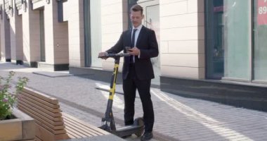 Heyecanlı erkek, elinde elektrikli scooterla ayakta duruyor, dışarıda dinleniyor.