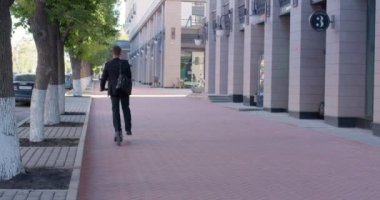 Şehirdeki cadde boyunca çalışmak için scooter kullanan bir iş adamı.