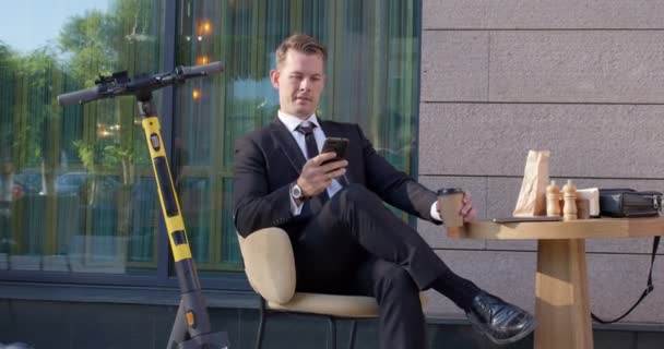 Приятный мужчина в костюме охлаждения в открытом кафе с помощью смартфона, питьевой кофе — стоковое видео