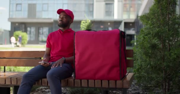 Afro americano consegna maschio sedersi in panchina a parlare con qualcuno, con borsa — Video Stock